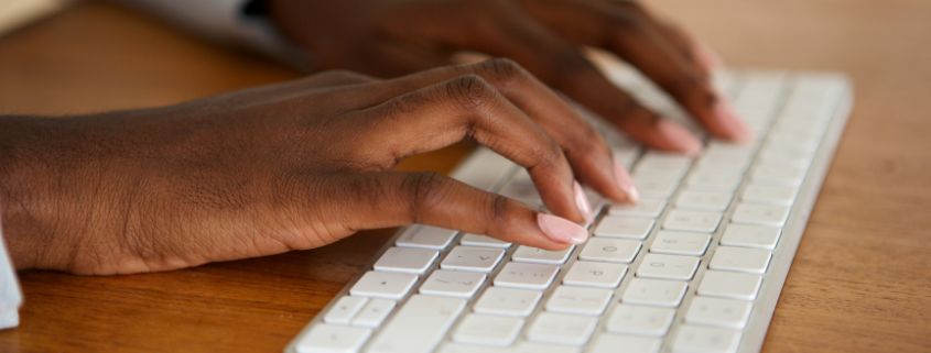 Hands typing on a computer keyboard sitting on a table