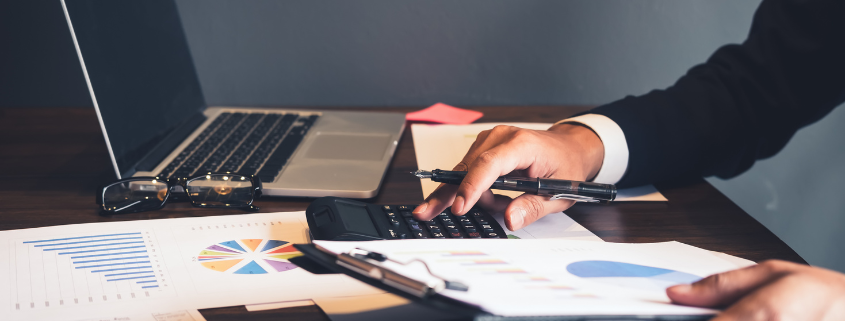 Man sitting at desk using computer and calculator with paperwork